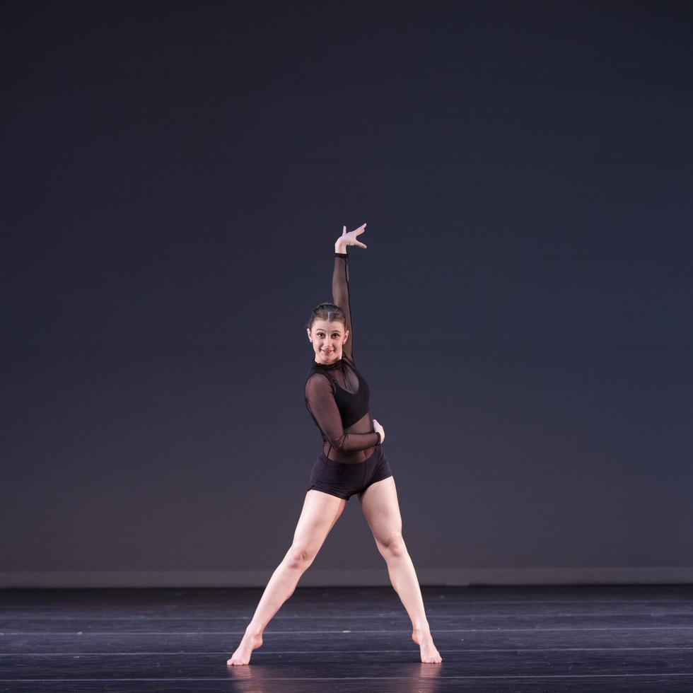 A dance student strikes a pose against a dark background on stage.