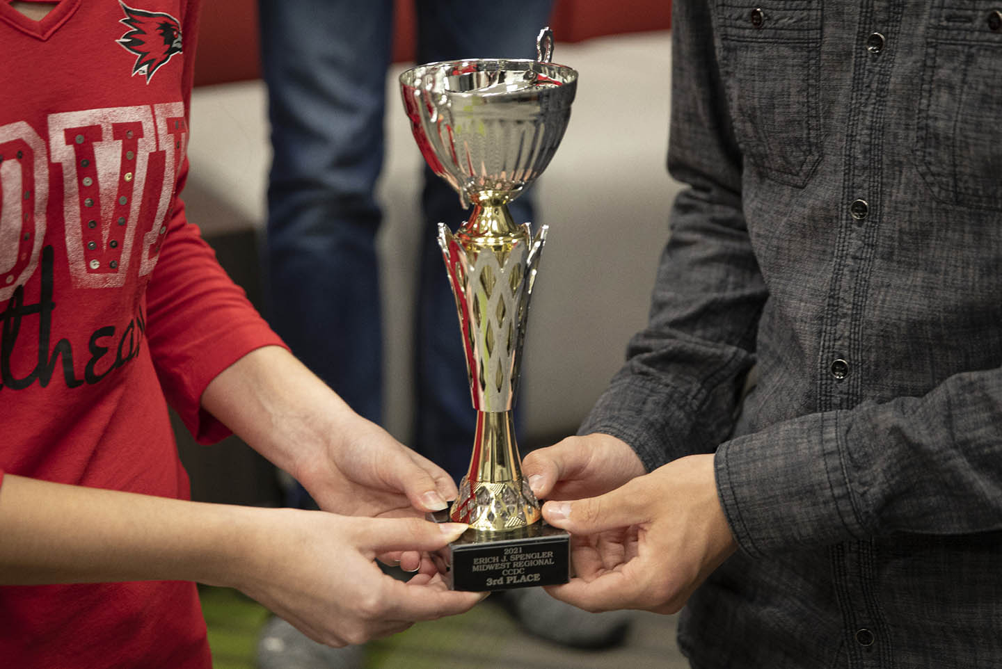 two cybersecurity degree students and cyber defense team members hold a trophy up for the photographer